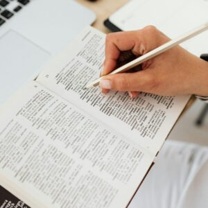 Close-up of a person underlining text in a dictionary on a desk with a laptop.